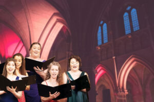 A group of singers wearing colourful evening gowns stand with their choir folders. The background is a vaulted church ceiling lit in Christmassy red tones.